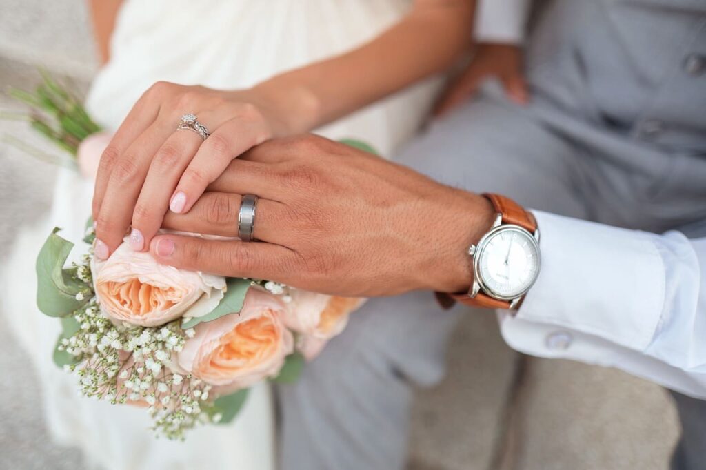 Nahaufnahme von Händen eines Hochzeitspaares mit Eheringen und Blumenstrauß