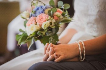 Braut hält Blumenstrauß und hält die Hand des Bräutigams während der Hochzeit